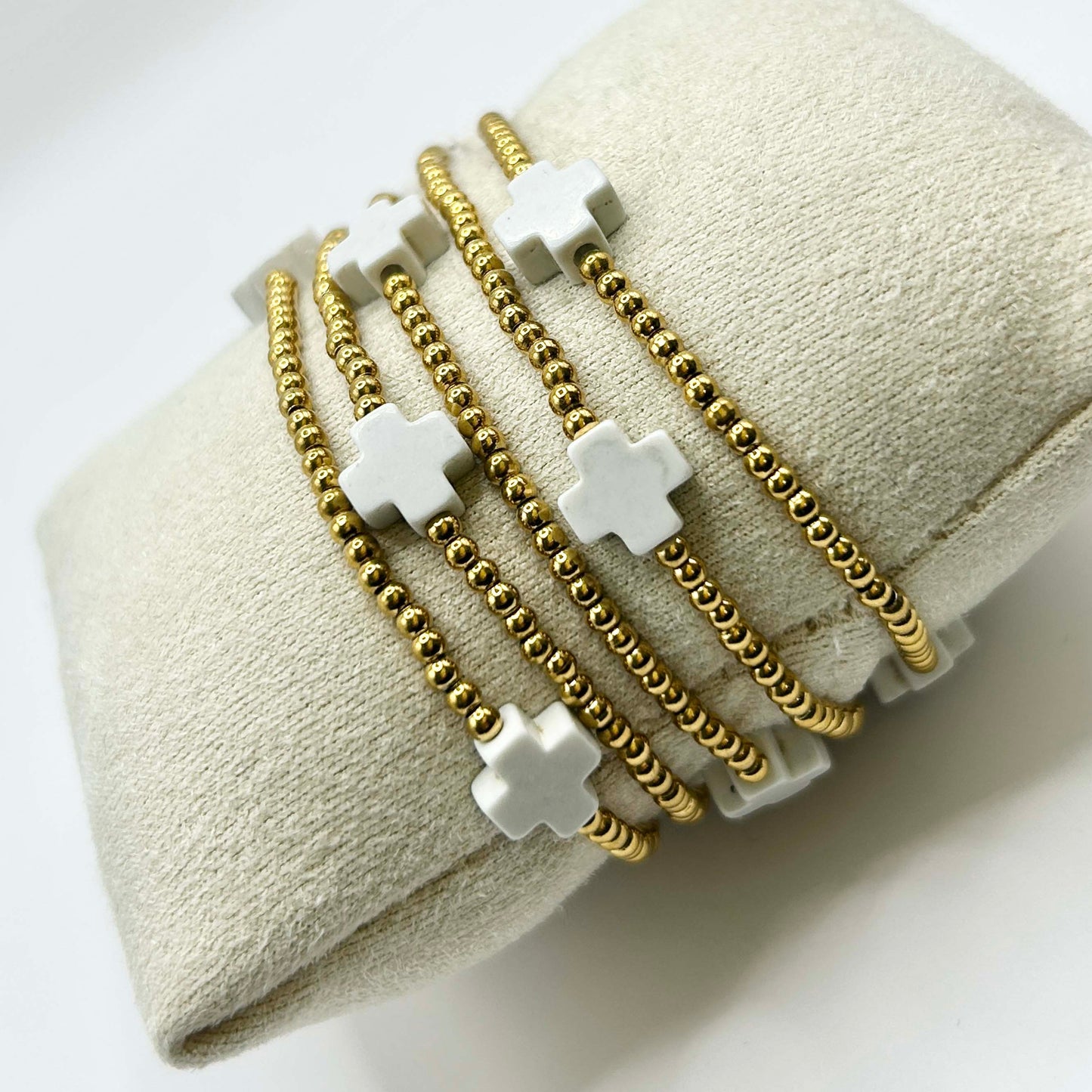 Zoomed-in view of the Leopoldine Divine bracelet featuring white cross-shaped stones and delicate gold beads, wrapped around a soft cushion for an elegant display.
