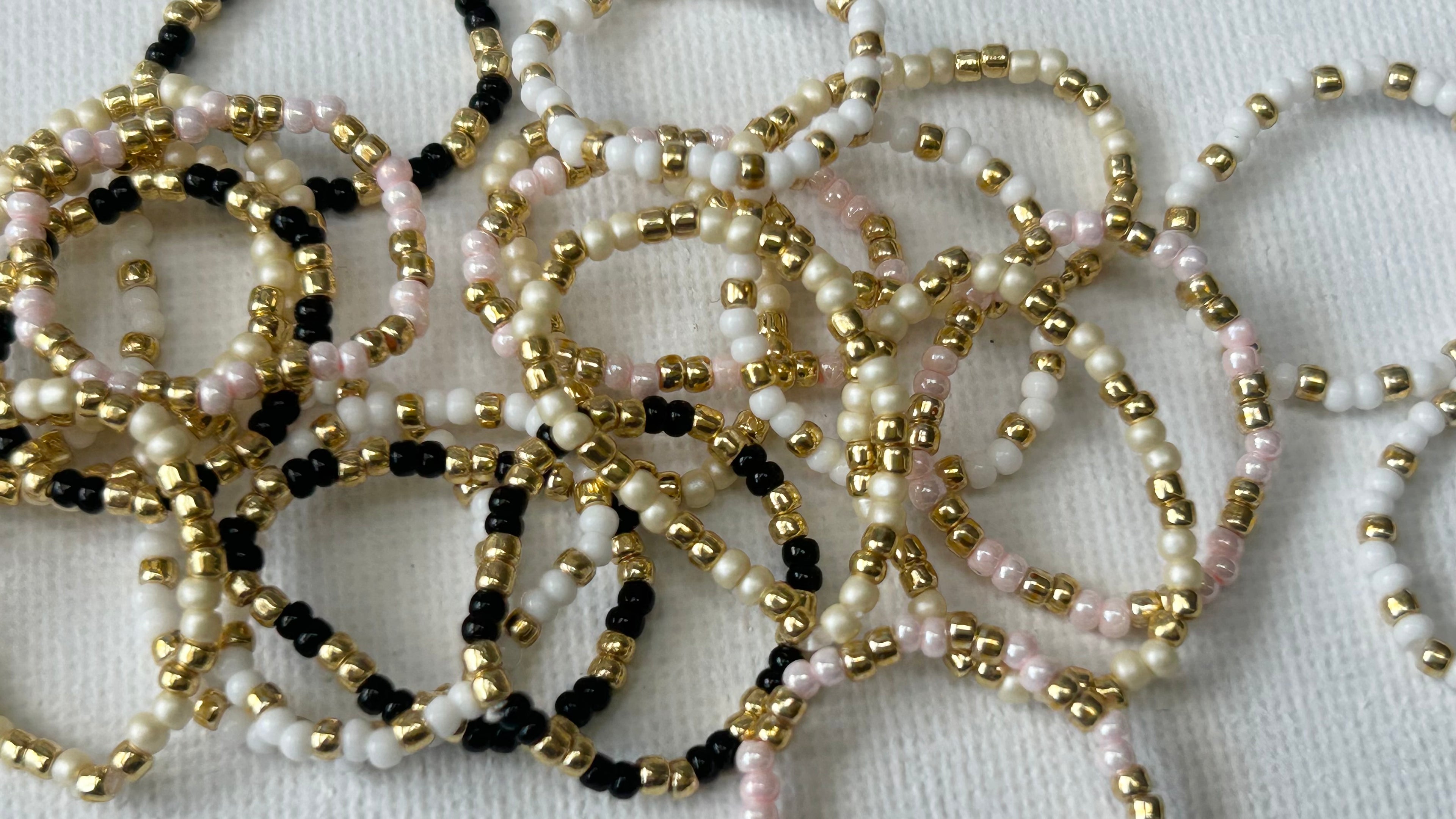 Affordable Confettis rings in white, pink, pearl and black beads with gold-tone details, scattered on white background – playful stackable jewellery UK.