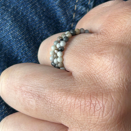 Close-up of grey Picasso gemstone stackable rings against denim, showcasing natural marbled texture.