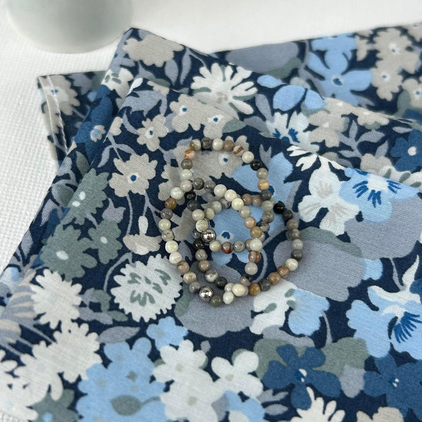 Trio of grey Picasso stone stackable rings laid on a blue Liberty London floral pouch, perfect as a stylish UK jewellery gift.