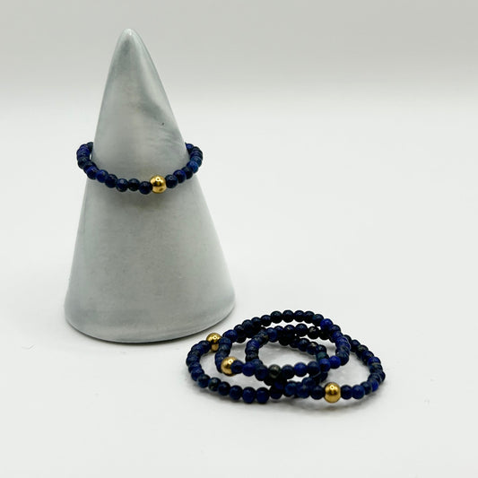 Affordable deep blue lapis lazuli ring with gold detail on ceramic holder, shown with matching stackable gemstone rings – minimalist jewellery UK.