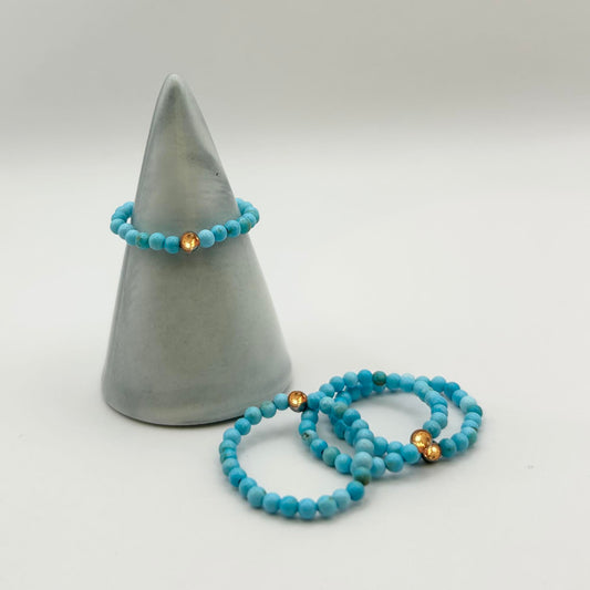 Minimalist stack of turquoise beaded rings with gold detail, styled on a ceramic cone – dainty affordable rings UK.